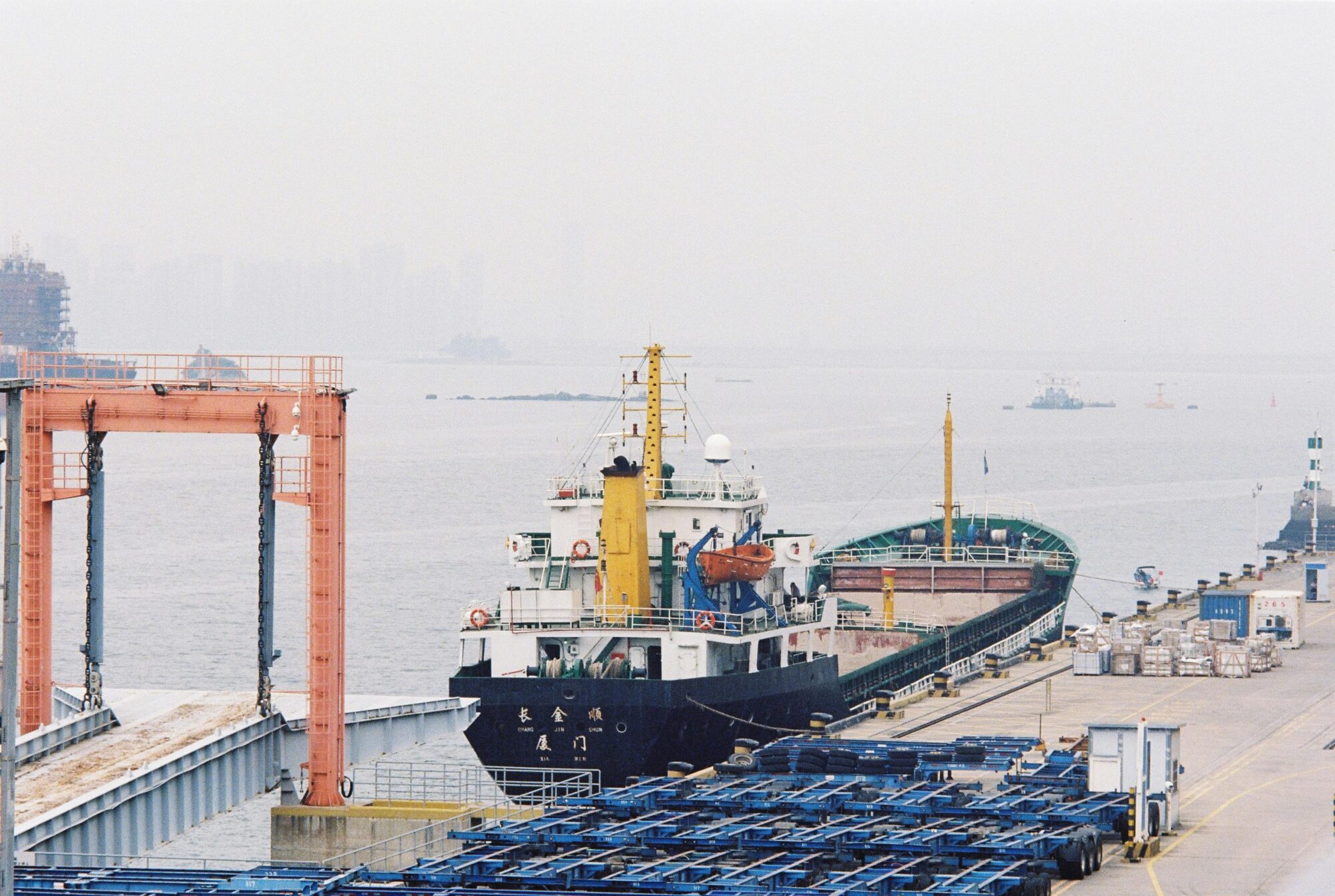 A cargo ship moored at an industrial harbor with cranes and containers for freight transport.